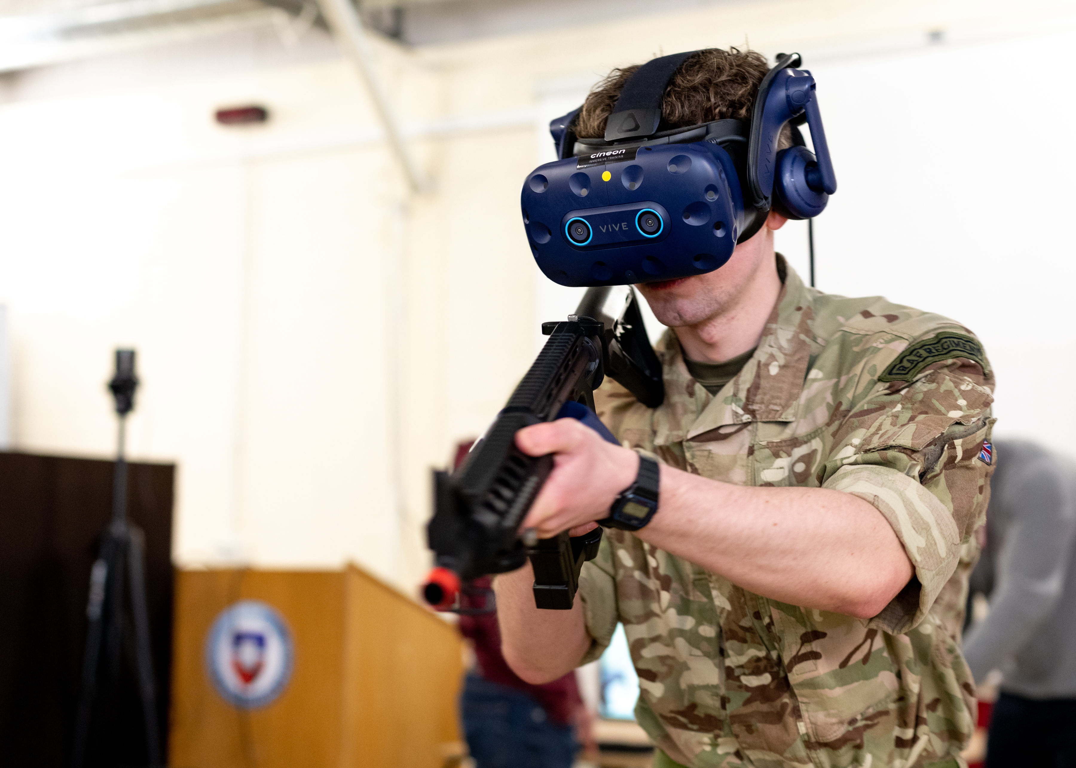 Personnel holds rifle while wearing virtual reality headset.